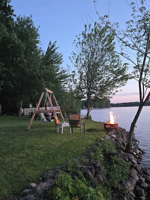 A lakeside setting with a swing set, a fire pit, and a view of the water.