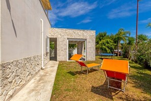 A building with a stone facade, a small patio area with two orange chairs, and a clear blue sky. - Spacious and comfortable 90 sqm villa, ideal for up to 4 guests, equipped with all the comforts for a relaxing holiday in the heart of Salento, including private parking, a large garden, a covered patio, and a furnished terrace, perfect for enjoying rela (Torre dell'Orso)