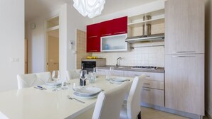 A modern kitchen with white cabinetry, a red upper cabinet, and a dining area with a white table and chairs. - Spacious and comfortable 90 sqm villa, ideal for up to 4 guests, equipped with all the comforts for a relaxing holiday in the heart of Salento, including private parking, a large garden, a covered patio, and a furnished terrace, perfect for enjoying rela (Torre dell'Orso)