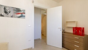 A room with a white door, a wooden dresser, and a wall with a framed picture. - Spacious and comfortable 90 sqm villa, ideal for up to 4 guests, equipped with all the comforts for a relaxing holiday in the heart of Salento, including private parking, a large garden, a covered patio, and a furnished terrace, perfect for enjoying rela (Torre dell'Orso)