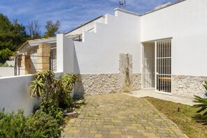 A modern house with a paved patio, stone wall, and a metal gate. - Spacious and comfortable 90 sqm villa, ideal for up to 4 guests, equipped with all the comforts for a relaxing holiday in the heart of Salento, including private parking, a large garden, a covered patio, and a furnished terrace, perfect for enjoying rela (Torre dell'Orso)