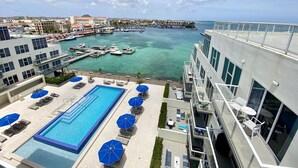 Una piscina sul tetto con lettini e ombrelloni, un porto turistico con barche e vista sulla città.