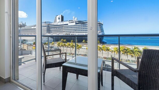 Un balcone con due poltrone in vimini e un tavolino, con vista su una spiaggia e una nave da crociera.