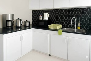 Una cocina moderna con armarios blancos, encimera negra, cafetera, hervidor, microondas, escurreplatos y un lavabo.