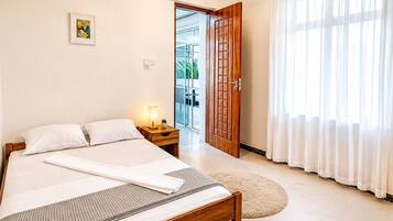 Ein Hotelzimmer mit einem Bett, einem Nachttisch, einer Tür zu einem Balkon und einem großen Fenster mit Vorhängen.