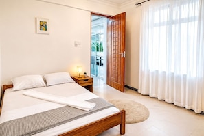 A hotel room with a bed, a nightstand, a door leading to a balcony, and a large window with curtains.