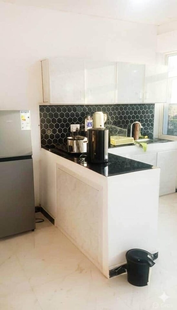 Una cocina con encimera negra, armarios blancos, un refrigerador de acero inoxidable y una olla negra en el suelo.