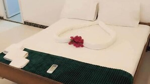 Siististi pedattu sänky, jossa on vihreä päiväpeite, valkoiset tyynyt ja punainen kukka koristeena.