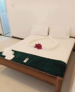 Una cama bien hecha con una colcha verde, almohadas blancas y una decoración floral roja.