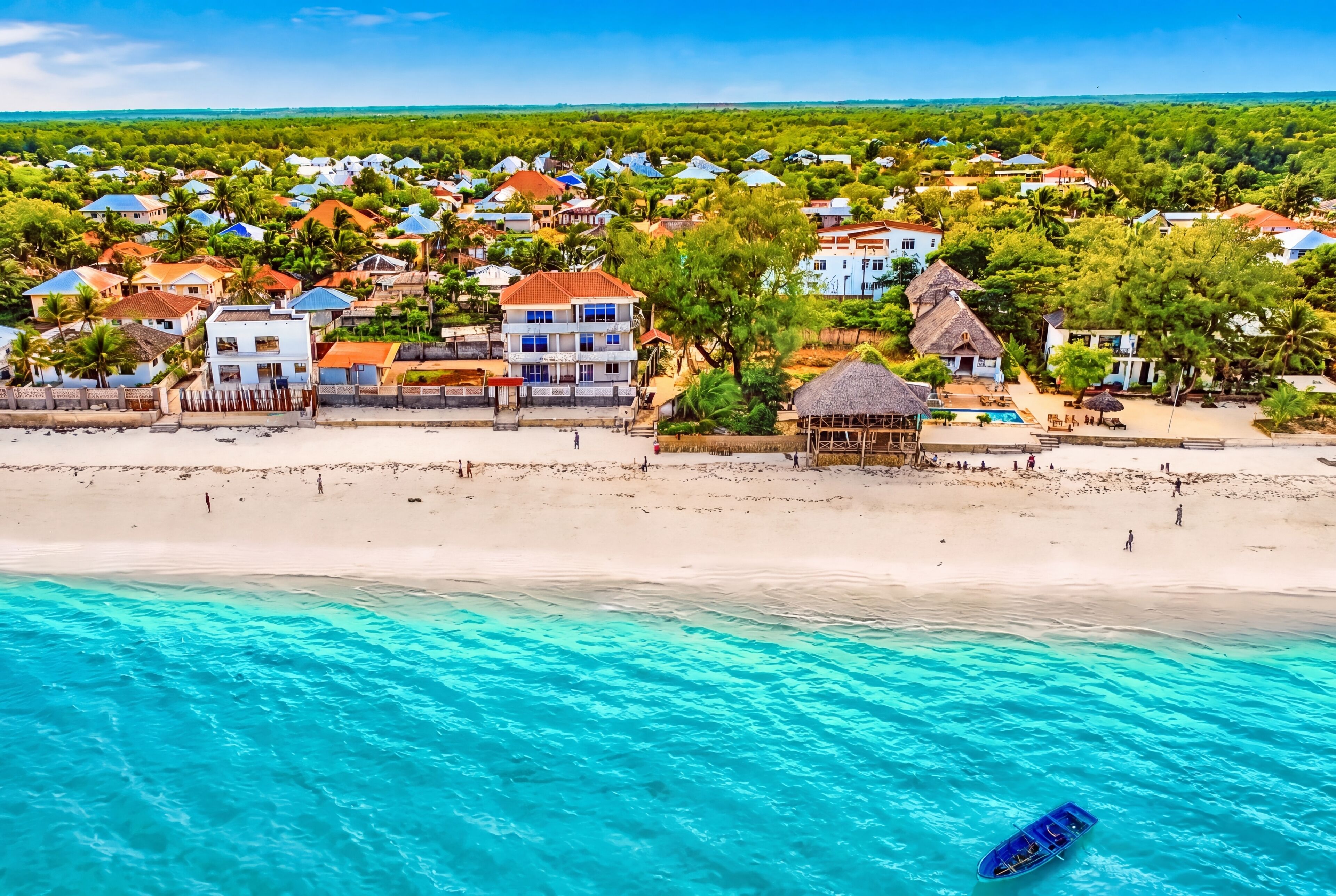 A coastal town with beachfront properties, clear turquoise waters, and a small boat on the sand.