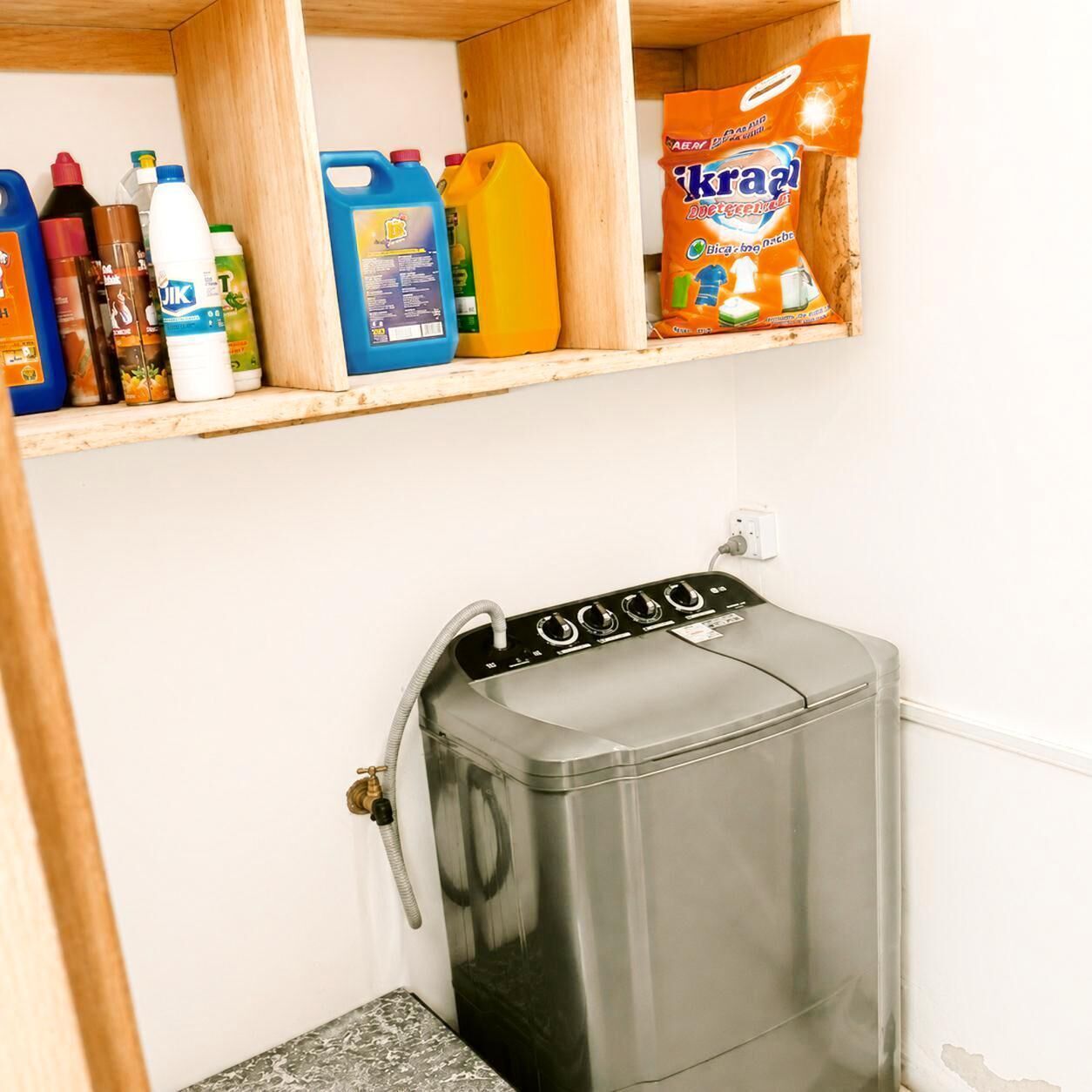 Un espace buanderie compact comprenant un lave-linge et un sèche-linge en acier inoxydable, une étagère pour les produits de nettoyage et un petit plan de travail.