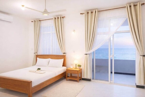A bedroom with a bed, bedside table, lamp, and a view of the sea through a sliding glass door.