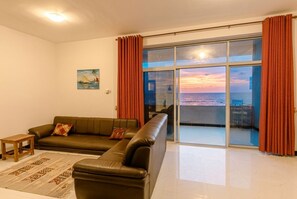 A living room with a sofa, a small table, and a view of the sea through a sliding glass door. - Beachfront Bliss with Stunning Ocean Views (Uroa)