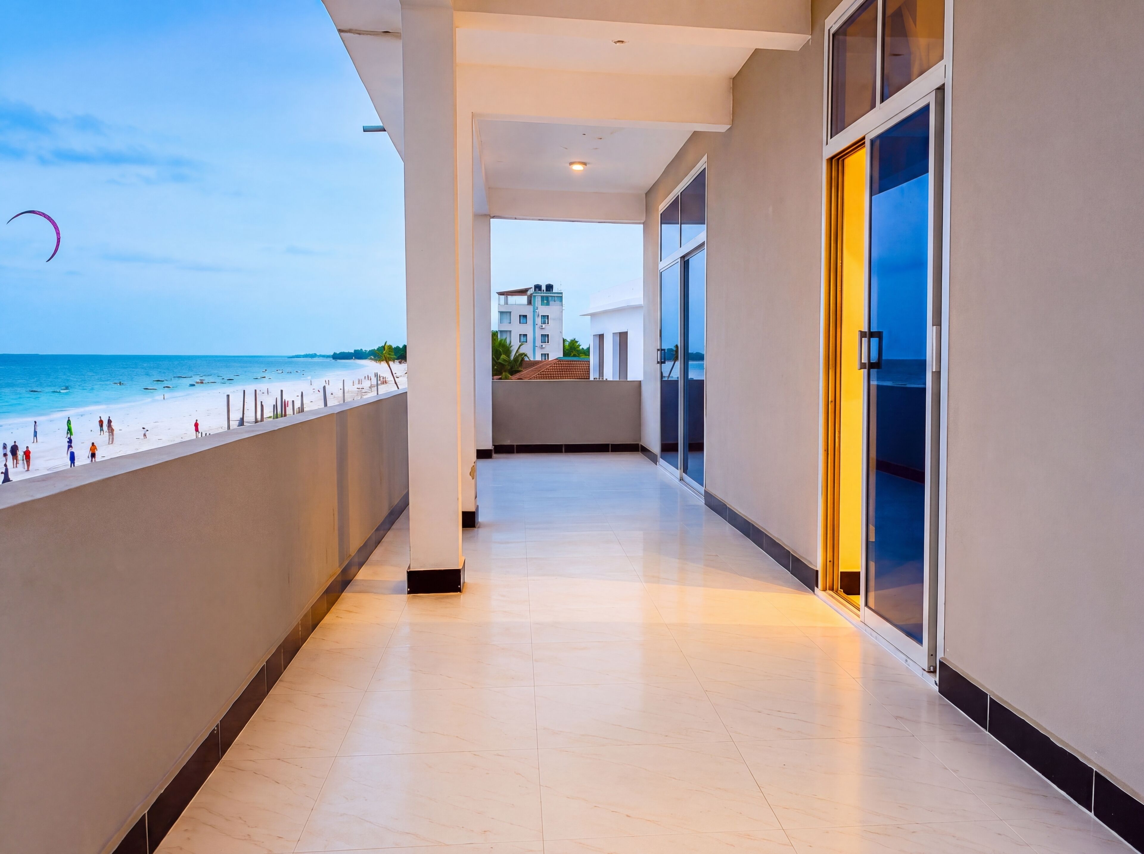 Pasillo con vista a la playa y al océano, que conduce a un edificio con amplios ventanales.