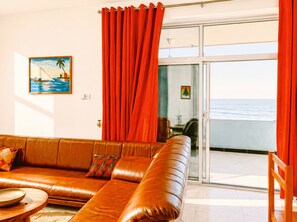 Une pièce comprenant un canapé en cuir, une table à manger et une vue sur la mer, accessible par une porte-fenêtre coulissante.