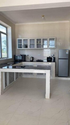 Una cocina moderna con encimera de mármol, armarios empotrados, refrigerador y ventana que proporciona luz natural.