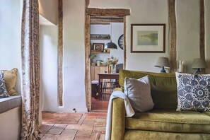 Ein gemütliches Wohnzimmer mit einem grünen Sofa, gemusterten Kissen, einem Holztisch mit einer Vase und einer Uhr an der Wand.
