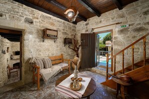 Interior rústico de pedra com escadaria de madeira, um banco e uma mesa com objetos decorativos.
