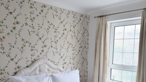 Een net opgemaakt bed met witte lakens, een grijs gewatteerd sprei en twee opgevouwen witte handdoeken.