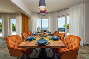 A dining room with a wooden table, orange upholstered chairs, and a view of the ocean.