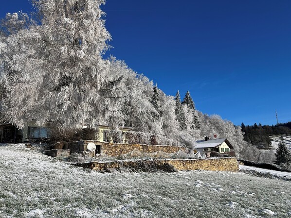 Ein Steingebäude mit einer Steinsäule, umgeben von schneebedeckten Bäumen und wolkenlosem, blauem Himmel.