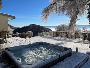 Ein Whirlpool in einer verschneiten Außenanlage mit freiem Blick auf einen bewaldeten Hügel im Hintergrund.