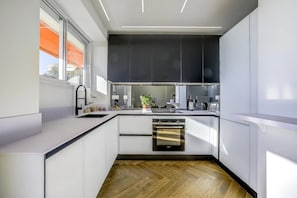 A modern kitchen with white cabinetry, a built-in oven, and a window with an orange awning. - Perfect 2-Bedroom Apartment with AC, Sea View & Terrace in Charming Nice, Garage (Nice)