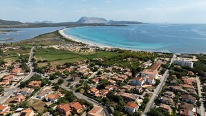 An aerial view of a coastal town with residential areas, a beach, and a mountain in the background.