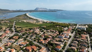 An aerial view of a coastal town with residential areas, a beach, and a mountain in the background. - Casa del Leccio F4/1 by Wonderful Italy (San Teodoro)