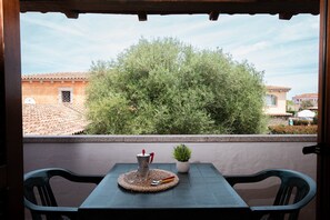 A balcony with a table, chairs, a coffee pot, a small potted plant, and a view of buildings and trees. - Casa del Leccio F4/1 by Wonderful Italy (San Teodoro)