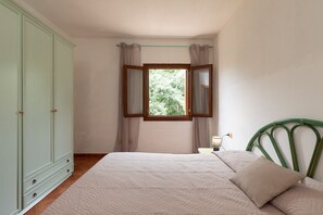 A bedroom with a bed, a wardrobe, a window with curtains, a bedside lamp, and a green headboard. - Casa del Leccio F4/1 by Wonderful Italy (San Teodoro)