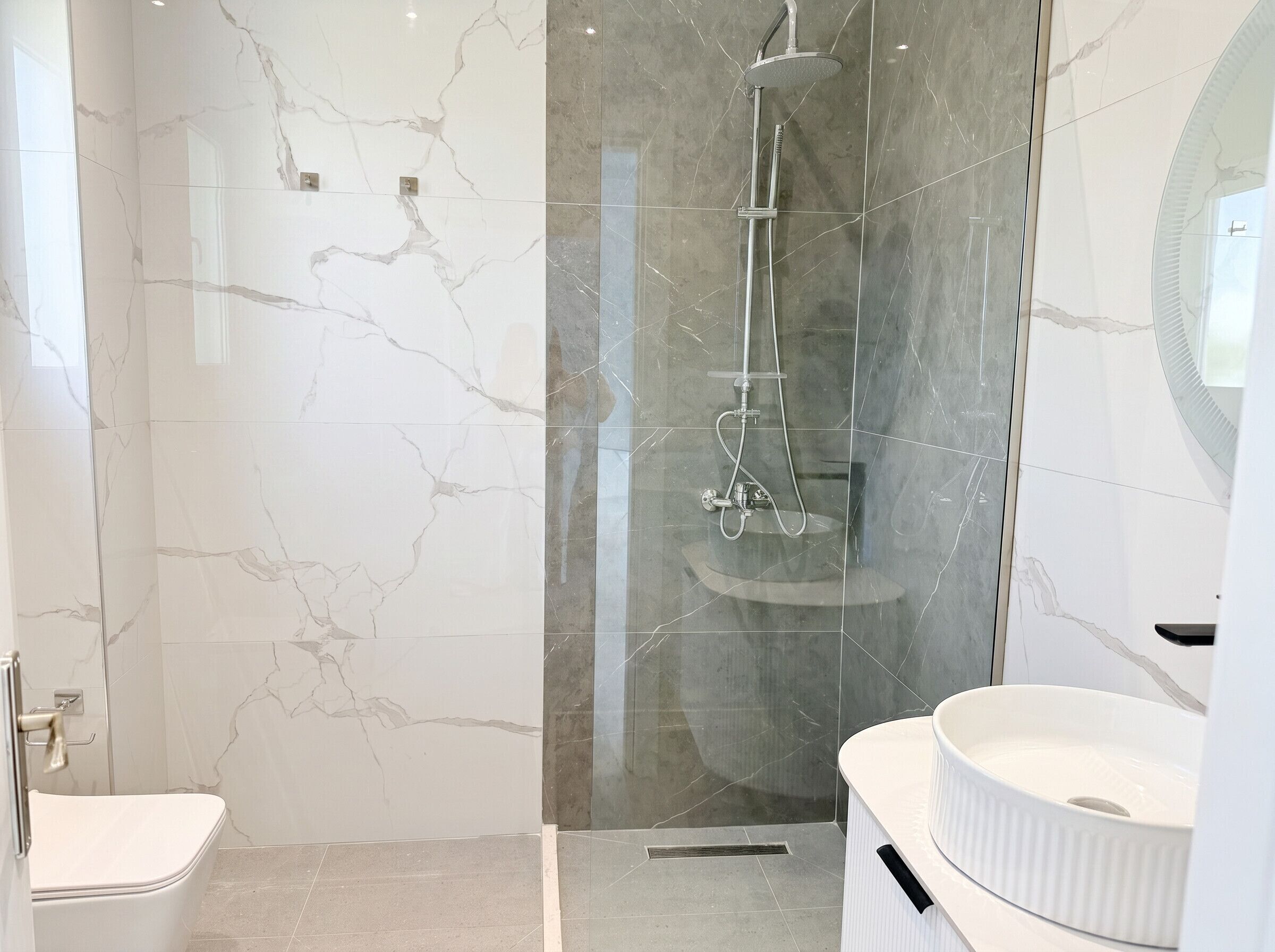 A modern bathroom with a glass-enclosed shower, a white sink, and marble walls.