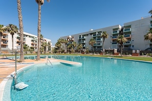 Ein Schwimmbad mit klarem, blauem Wasser, umgeben von Palmen und modernen Apartmentgebäuden.