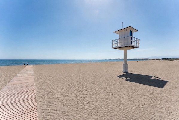 Ein Rettungsschwimmturm am Strand, verbunden durch eine Holzpromenade.