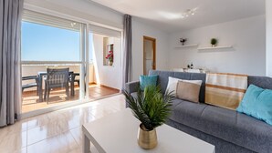 A modern living room with a sofa, a coffee table, and a balcony with a table and chairs. - AlmeriaSuite Palm Beach Golf & Pool 7301 (El Ejido)