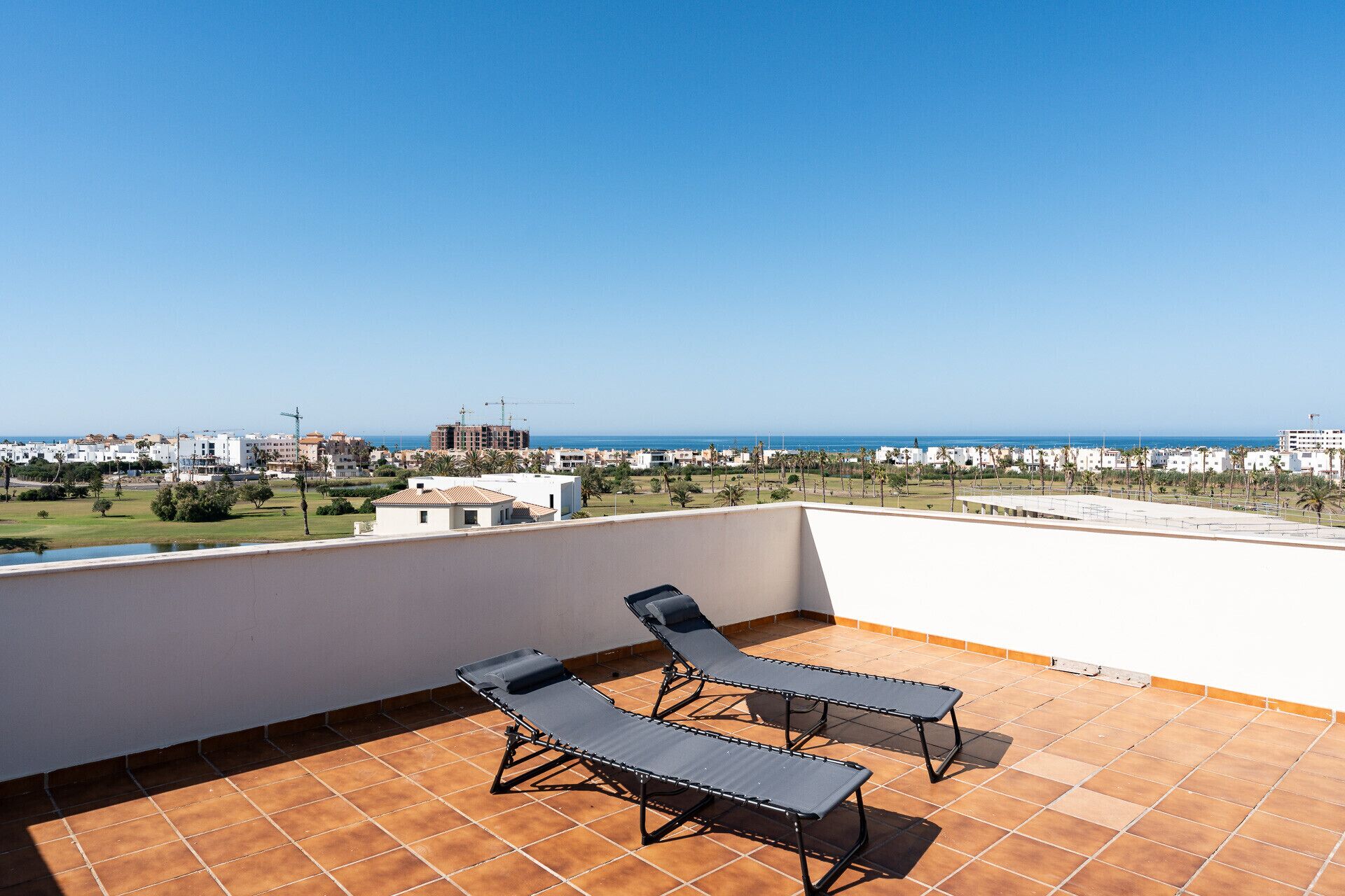 Une terrasse avec deux fauteuils et une vue sur la mer et les bâtiments.