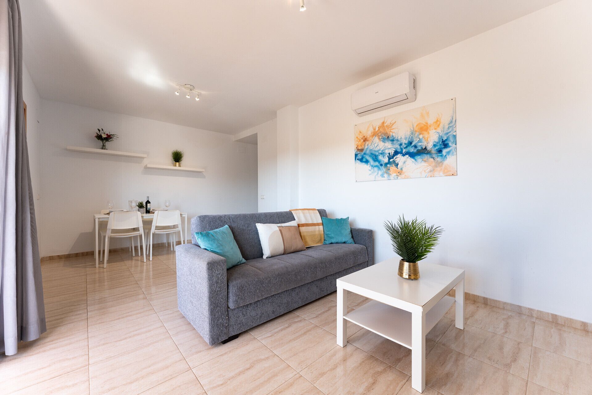 Un salon moderne avec un canapé gris, une table basse blanche et un coin repas comprenant une table et des chaises blanches.