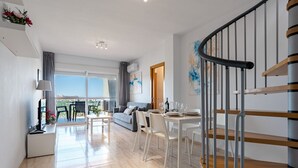 En modern lägenhet med ett matområde, en soffa, en trappa och utsikt genom stora fönster.