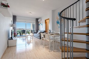 Eine moderne Wohnung mit Essbereich, einer Couch, einer Treppe und Blick durch große Fenster.