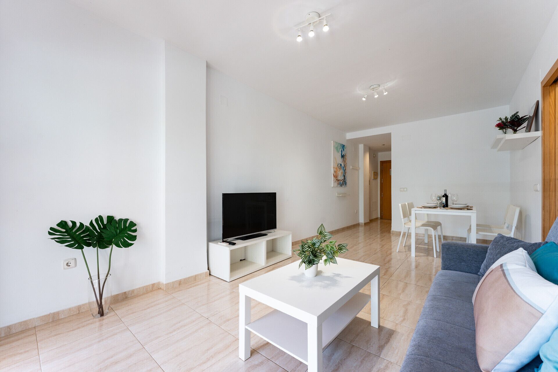 A modern living room with a flat-screen TV, a white coffee table, and a sofa.