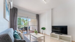 A modern living room with a sofa, a coffee table, a TV on a stand, and a balcony with a view of palm trees. - AlmeriaSuite 2005 P Palm Beach (El Ejido)