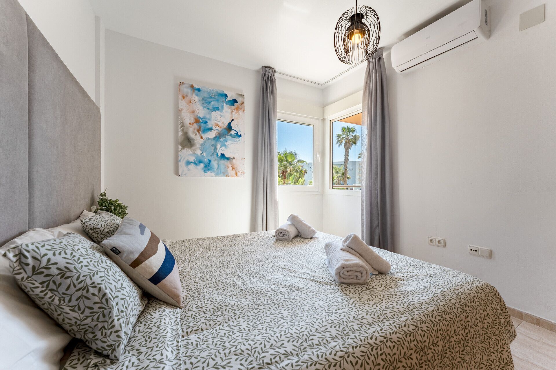 Une chambre à coucher avec un lit, des oreillers, un tableau, une fenêtre et un appareil de climatisation.