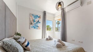 A bedroom with a bed, pillows, a painting, a window, and an air conditioning unit. - AlmeriaSuite 2005 P Palm Beach (El Ejido)