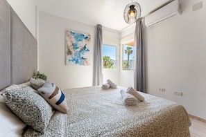 Ein Schlafzimmer mit Bett, Kissen, einem Gemälde, einem Fenster und einer Klimaanlage.
