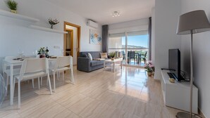 Un soggiorno moderno con zona pranzo, un divano grigio, una TV e un balcone con vista.
