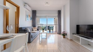 Un soggiorno moderno con divano, televisione, tavolo da pranzo e balcone con mobili da esterno.