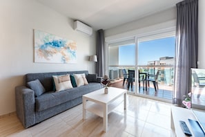 Una sala de estar moderna con un sofá gris, una mesa de centro blanca y un ventanal con vistas a edificios.
