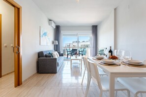 Ein modernes Wohnzimmer mit grauem Sofa, einem Esstisch für zwei Personen und Blick auf die Stadt durch große Fenster.