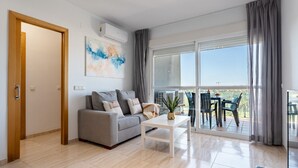 Un salon moderne avec un canapé gris, une table basse blanche et une grande fenêtre donnant sur l’extérieur.