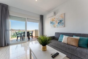 A modern living room with a grey sofa, a coffee table with a plant, a remote control, and a painting on the wall. - AlmeriaSuite Palm Beach Golf & Pool 6303 (El Ejido)